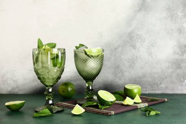 Soğuk mojito bardakları, nane yaprakları ve limonlar ışık duvarına karşı renk masasında.