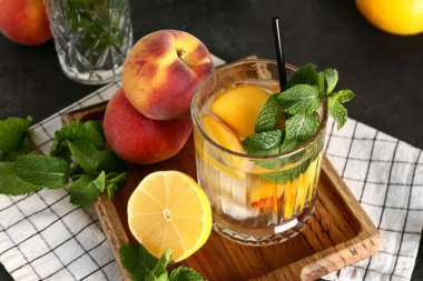 Bir bardak taze şeftalili limonata ve siyah masada nane şekeri.