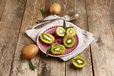 Dilimlenmiş taze kivi ve ahşap arka planda yapraklar.