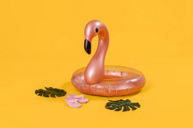 Flamingo şeklinde şişirilebilir halka, palmiye yaprakları ve pembe arka planda parmak arası terlikler.