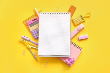 Sarı zemin üzerinde boş defter ve okul kırtasiyesi olan kompozisyon