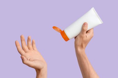 Leylak arka planında güneş kremi şişesi olan kadın elleri.