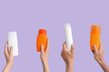 Leylak arka planında güneş kremi şişeleri olan kadın elleri.