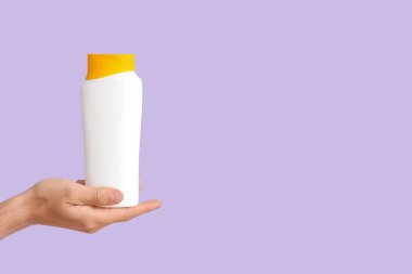 Leylak arka planında güneş kremi şişesi olan bir kadın eli.