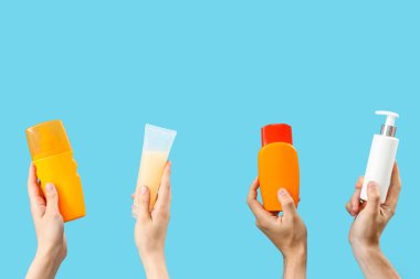 Mavi arka planda güneş kremi şişeleri olan kadın elleri