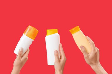 Kırmızı arka planda güneş kremi şişeleri olan kadın elleri.