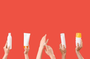 Kırmızı arka planda güneş kremi şişeleri olan kadın elleri.