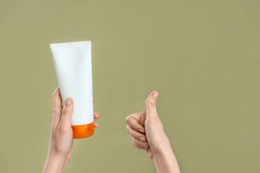Güneş kremi şişesi olan kadın elleri yeşil arka planda baş parmağını gösteriyor.