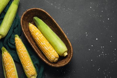 Siyah arka planda taze mısır koçanları olan hasır bir kase.