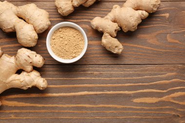 Taze zencefil kökleri ve ahşap zemin üzerinde kurumuş toz bulunan bir kase.