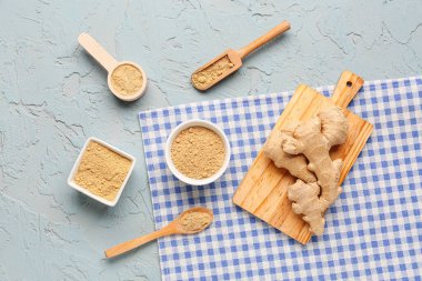 Taze zencefil kökü, kâseler ve mavi zemin üzerinde kurutulmuş toz bulunan tahta kaşıklar.