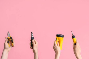 Electrician hands with tools on pink background