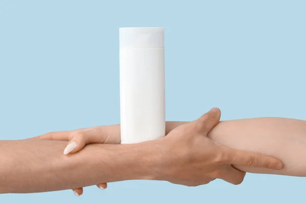 Female hands with bottle of sunscreen cream on blue background