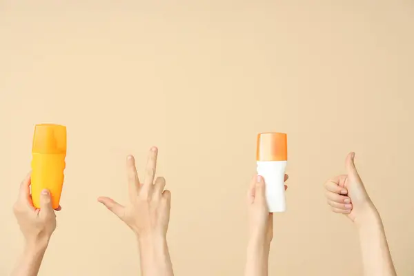 Female hands with bottles of sunscreen cream showing victory and thumb up gestures on beige background