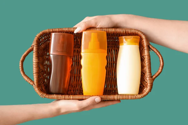Female hands with bottles of sunscreen cream in basket on green background