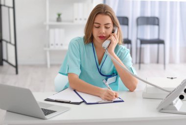 Klinikteki iş yerinde telefonla konuşan kadın bir tıp asistanı.