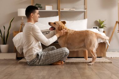 Yatak odasında Labrador köpeği olan genç bir adam.