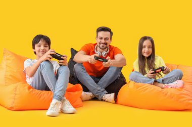 Baba ve küçük çocukları sarı arka planda video oyunu oynuyorlar.