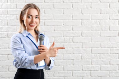 Beyaz tuğlalı arka planda bir şeye mikrofonlu kadın gazeteci