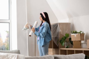 Genç bir kadın taşınma gününde evinde streç filmle lambayı paketliyor.