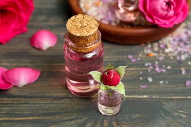 Gül özü ve ahşap masa üzerinde çiçekler olan kozmetik yağı şişeleri.