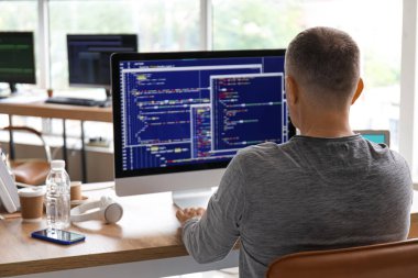 Olgun erkek programcı iş yerindeki ışık ofisinde oturuyor.