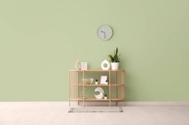 Odadaki yeşil duvarda ev bitkileri ve saati asılı modern raf ünitesi.