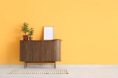 Çağdaş çekmeceler, içinde ev bitkileri ve turuncu duvarın yanındaki boş resim.