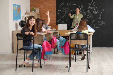 Sırt çantalı küçük öğrenciler sınıfta ders alıyorlar.