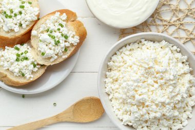Süzme peynirli ekmek parçaları ve beyaz ahşap masada ekşi krema.