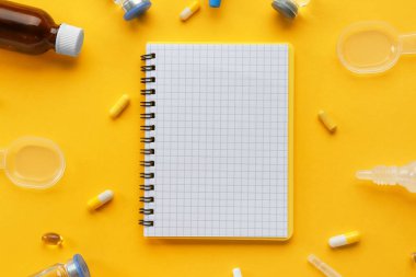 Sarı arka planda not defteri ve haplarla kompozisyon
