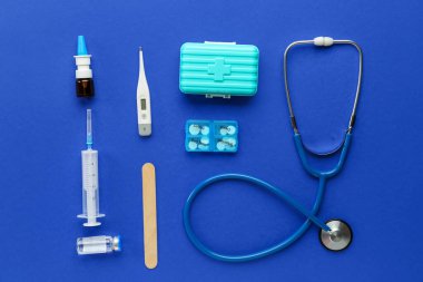 Tıbbi steteskop, şırınga, ilk yardım çantası ve mavi arka planda ilaç kutusu.