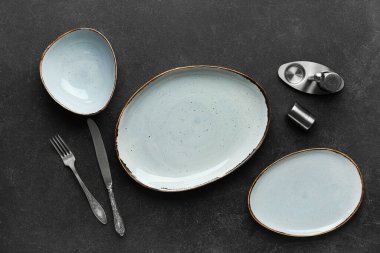 Temiz tabaklar, çatal bıçak takımı ve tuzluk siyah masada.