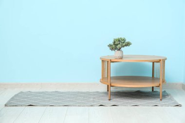 Bonsai ağacıyla ahşap masa ve mavi duvarın yanında şık bir halı.