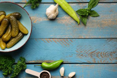 Mavi ahşap arka planda salatalık turşusu ve farklı baharatlarla dolu bir kase.