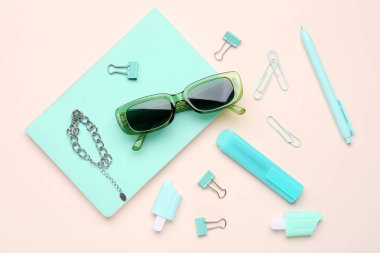 Kırtasiye malzemeleri ve pembe arka planda zincirli güneş gözlüğü.