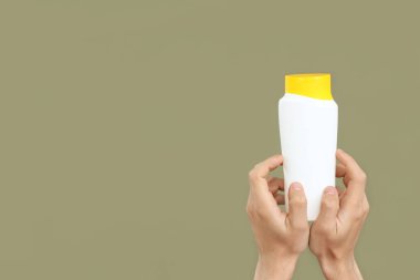 Yeşil arka planda güneş kremi şişesi olan kadın elleri