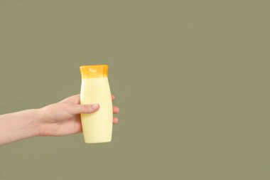 Yeşil arka planda güneş kremi şişesi olan bir kadın el.