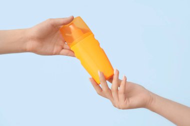 Mavi arka planda güneş kremi şişesi olan kadın elleri.