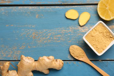 Taze zencefil kökü, limon ve kase mavi ahşap arka planda kurutulmuş toz.
