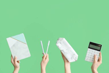 Female hands with school accessories on green background