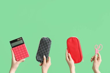 Female hands with school accessories on green background