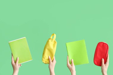 Yeşil zemin üzerinde kalem kılıfları ve defterleri olan kadın elleri