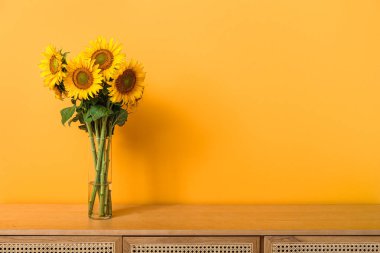 Turuncu duvarın yanındaki masada güzel ayçiçekleri olan vazo.