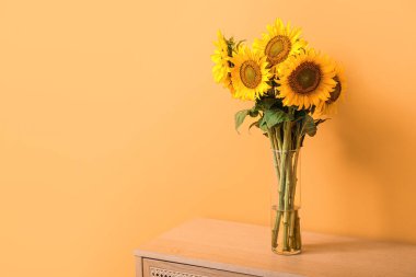 Turuncu duvarın yanındaki masada güzel ayçiçekleri olan vazo.