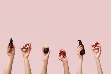 Pembe arka planda kozmetik ürünleri ve nar tutan kadın eller