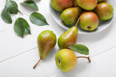 Beyaz ahşap masada olgun armutlarla dolu bir tabak.