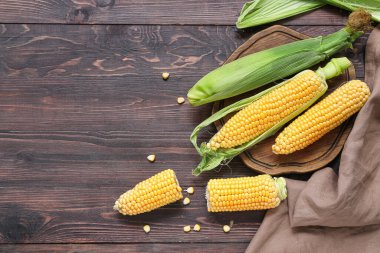 Koyu ahşap masada taze mısır koçanları.