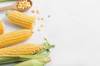 Taze mısır koçanları ve beyaz masada çekirdekli ahşap kaşık.