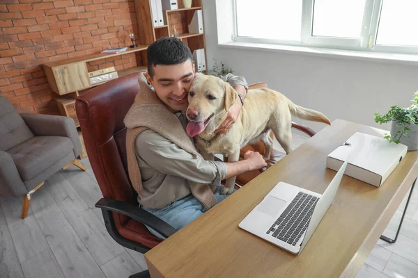 オフィスのテーブルでかわいいラブラドール犬を抱擁する若い男 — ストック写真